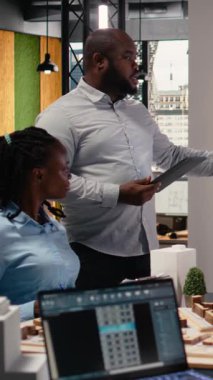 Dikey Video Afrikalı Amerikalı emlak mühendisi ekiple işbirliği sırasında 3D modeller üzerinde site hazırlama planı ve imar düzenlemelerini sunuyor. Şehir planlaması için konut girişimi