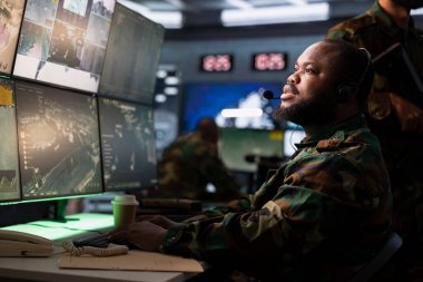 Hava savunmasından sorumlu memur, kulaklık mikrofonuyla sınırlarda devriye gezen filolara talimatları iletiyor. Afrika kökenli Amerikan askeri istihbarat ajanı birliklerle iletişim kuruyor.