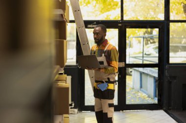 Siyah personel küçük bir depoda ürün perakende envanteri düzenliyor, e-ticaret sevkiyatları için karton kutular hazırlıyor ve ulaşım lojistiği ile ekspres teslimatı destekliyor..