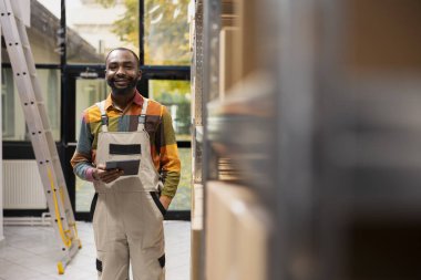 Küçük ölçekli depo için karton kutuları kontrol eden siyah bir çalışanın portresi, ürün perakende siparişleri ve sevkiyat hizmeti operasyonları. E-iş etkinliği.