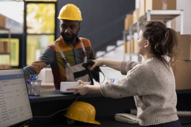 Bir depolama tesisinde çalışanlar malları işlemek için barkod tarayıcı kullanırlar, doğru envanter kontrolü ve ürün işleme ile uygun nakliye hizmeti ve e-ticaret dağıtımını sağlarlar.
