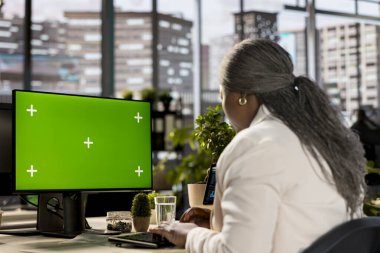 Siyahi kadın işçi, kroma anahtarının yanındaki mali özeti okuyarak şirket için küresel kalkınma stratejisi üzerinde çalışıyor. Çalışan önemli web verilerini inceliyor.