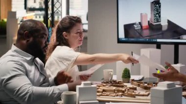 İnşaat düzeni seçeneklerini araştırmak için 3D modeller kullanan emlak ekibi, müteahhitlerle yapılan stratejik ofis toplantısında kentsel kalkınma aşaması için konut projesi üzerinde çalışıyor. Kamera B.