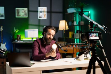 Stüdyodaki adam profesyonel kamera ve mikrofonla çevrimiçi yayın platformları için akıllı ampul incelemesi yapıyor. Çevrimiçi yıldız filmleri yüksek kaliteli ekipmanlı IoT ev otomasyon ürünü