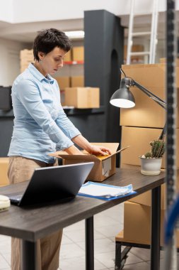 Warehouse employee managing factory operations in a local storage room, processing orders and handling packages to ensure efficient distribution of merchandise. Small business.