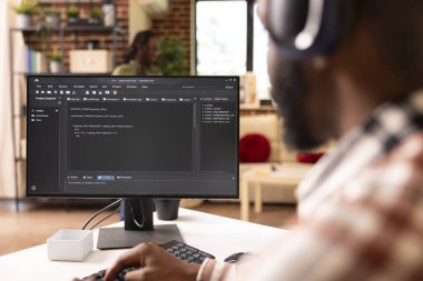 Web sitesi kodunu yazmak ve gözden geçirmek için masaüstü bilgisayarını kullanan Afro-Amerikan serbest kodlayıcısına yakın çekim. Siyah teknoloji girişimcisi evde bilgisayarla çalışıyor, programlama dilini hata ayıklıyor.