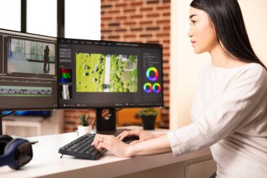 Female video editor arranges timelines and color grades raw footage with focus, bringing cinematic stories to life. Asian woman working remotely on film documentary in home studio.