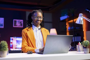 Upbeat remote worker in home office checking analytics statistical data sets on laptop. Cheerful African american teenager optimizing key performance indicators in apartment workspace