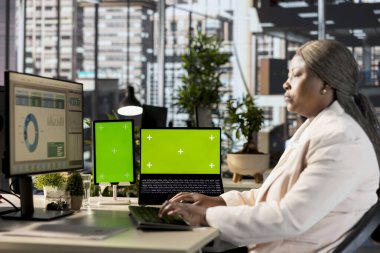 Siyahi kadın işçi, kroma anahtarının yanındaki mali özeti okuyarak şirket için küresel kalkınma stratejisi üzerinde çalışıyor. Çalışan önemli web verilerini inceliyor.