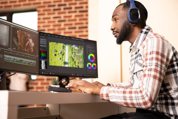 Sound editor working on cinematic content with headphones, creating and synchronizing audio files to montage. Black videographer applying color grading and finetuning transitions while enjoying music.
