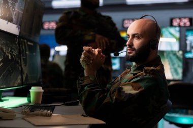 Military dispatcher in war room ready to respond to emergencies and communicate with soldiers on front lines. War telecommunications operator in uniform talking in device microphone