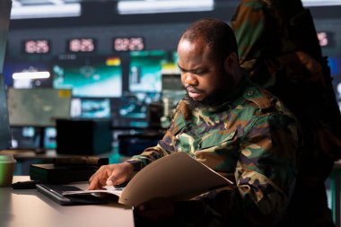 Military officer reviews battlefield information after conducting special operation reconnaissance, supporting field troops. Soldier reading mission case file, getting debriefed on enemies