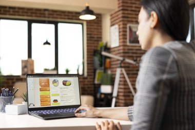 Ofis masasında oturan profesyonel bir kadın mevcut projeleri analiz ediyor ve yeni başlayanların hedeflerini hesaplıyor. Dizüstü bilgisayarda çalışan genç bir kadın, iş raporları hazırlıyor..