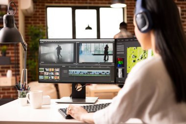 Evde kamera arkasında çalışan odaklanmış kadın film yapımcısı, görüntüleri düzenliyor ve görsel efektler ekliyor. İkili monitörlerde oturan Asyalı kadın kameraman zaman çizelgelerini ve sinematik çekimleri kontrol ediyor.