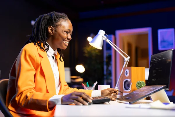 Cheerful engineer writes code on laptop while in apartment office, feeling excited after being successful. Overjoyed programmer celebrating fixing database errors while working from home