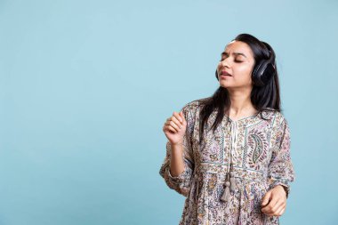 Kaygısız Hintli kadın müzik çalıyor ve etrafta geziniyor, döner tabloları kullanıyor gibi yapıyor ve ritimle dans ediyor. Neşeli DJ kulaklık takıyor, stüdyo arka planında ritim yapıyor..