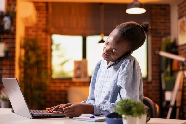 Siyahi kadın girişimci masada oturmuş, iş görüşmesi yapıyor ve dizüstü bilgisayardaki notları gözden geçiriyor, teknoloji ve iletişim becerilerini birleştiriyor. Evde cep telefonuyla konuşan Afrikalı Amerikalı kadın..