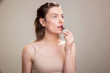 Yüzünde hafif bir parıltıyla stüdyoda poz veren, az makyajlı görünümü için ince ruj süren parlak bir kadın model. Parlak zarif kız makyaj ürünlerini tanıtıyor..