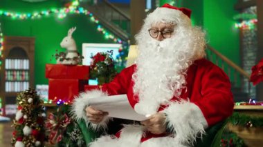 Noel Baba kılığındaki yaşlı adam çocuklardan hediye isteyen bir mektup aldı. Noel süslü odada Noel Baba kostümü giyen yaşlı kişi çocuklardan mektup okuyor, kamera A