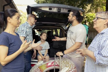 Open trunk and the baggage ready as large family group pack for holiday, grandparents and young parents with their little child prepare the car for road trip. Laughter and love under the sun.