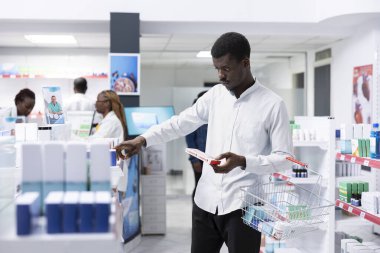 Black customer looking at cardiology pills and vitamins for prevention, reading boxes labels in the pharmacy shop. Evaluating options for healthcare treatment in a busy drugstore.