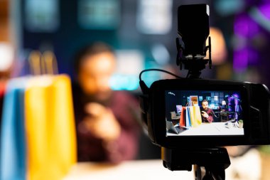 Medya yıldızlarının elinde renkli alışveriş torbaları tutarak video bloğu çekerken kullandıkları profesyonel kameranın yakın çekimi. İçerik oluşturucu tarafından bulanık arkaplanda kullanılan özelleştirilmiş teçhizata odaklan