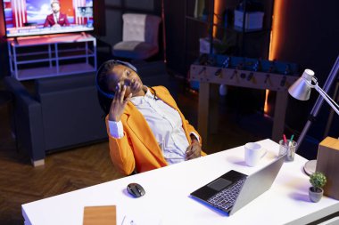 Woman wearing headphones sleeping at desk while watching TV programs on laptop at home. Person falling asleep on chair in living room after looking at television series late at night on notebook