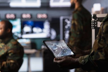 Dijital cihazdaki hava keşif verilerini inceleyen bir asker savaş kazanma taktikleri geliştirdi. Tablet kullanarak İHA 'ları kontrol eden ajan stratejik düşman hedeflerine saldırıyor.