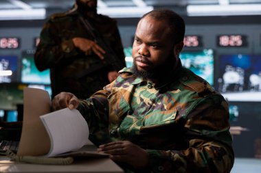 Military agent in command center browsing through intel folder files to learn about enemy battle formation. Intelligence agency officer in army headquarters reading mission case file