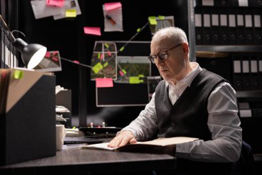 Male private inspector studying forensic evidence on case files in an incident room, collecting proof for police enforcement and making connections between illegal operations and suspects.