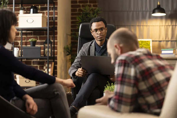 Odaklanmış terapist perişan bir çiftin karşısında dizüstü bilgisayarla oturup ilişki sorunlarını dinliyor. Karı koca arasındaki evlilik anlaşmazlığını değerlendiren Afrikalı Amerikalı psikolog portresi.