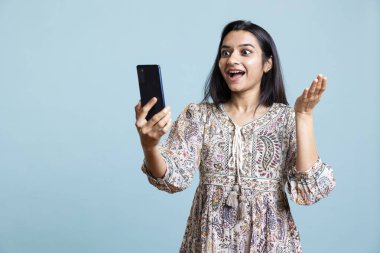 Kendinden geçmiş genç bir yetişkin telefonda arkadaşlarıyla sohbet etmekten mutlu olur, dostça jestler yapar ve el sallar. Neşeli Hintli kadın stüdyoda akıllı telefonuyla telekonferansa katılıyor..