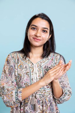 Mavi arka planı alkışlayan ve başarı için tezahürat yapan neşeli iyimser kişi, kişisel başarı için ayakta alkışlanıyor. Hintli kız hayranlık içinde stüdyoda el çırpıyor..