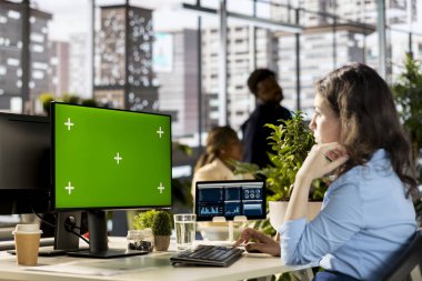 Genç kadın analist yeşil ekranın yanındaki çevrimiçi raporlar üzerinde çalışıyor, iş geliştirme için bir sunum oluşturmak için yıllık bilgi ve performans ölçümlerini kullanıyor. Şirket ofisi..