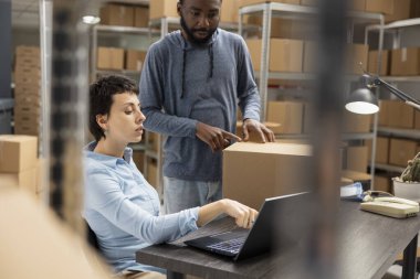 Diverse warehouse workers focusing on custom orders and package tracking in a tightly organized shipping space designed for small business logistics and merchandise hand packing.