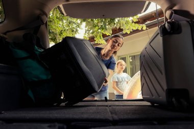 Small family of two share a cheerful moment loading the car trunk with essentials for their seaside vacation. Mom and child enjoying a summer getaway with laughter and relaxation together.