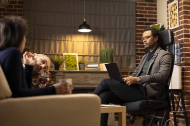 Couple attends counseling session in psychiatrist office as therapist listens attentively and takes digital notes. Unhappy spouses discuss marriage struggles, seeking guidance for recovery and balance