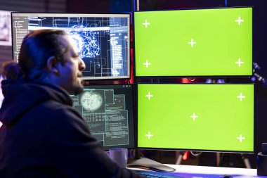 Hacker doing covert operations using green screen PC to bypass advanced security barriers. Rogue programmer in neon apartment engineering data theft script to penetrate firewalls using mockup computer