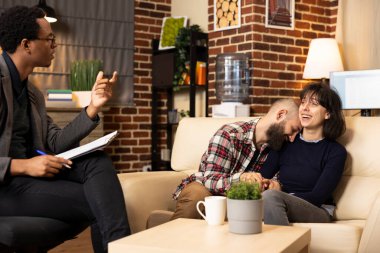 Terapi sırasında kanepede sarılıp gülüşüp barışma anlarını paylaşan beyaz bir çift. Erkek arkadaş ve kız arkadaş el ele tutuşuyor, profesyonel danışmandan olumlu geri bildirim alıyor..