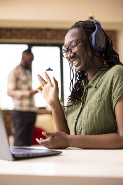 Siyah kadın serbest çalışan dizüstü bilgisayara selam veriyor, online beceri toplantısına katılıyor. Gülümseyen Afrikalı Amerikalı kadın uzaktan iş arkadaşlarına dostça el sallayarak sanal bir buluşma başlattı..