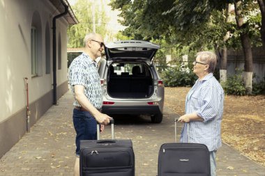 Senior couple loading the car trunk with luggage and being excited as they prepare for a relaxing road trip vacation. Retired duo enjoys travel and a happy lifestyle outdoors together.