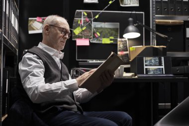 Old commissioner gathering information from case files in police incident room, arranging witness statements and confidential data. Solving criminal activity for a law enforcement operation.