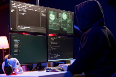 Hooded hacker in underground HQ coding malware designed to exploit network backdoors, Rogue programmer bypassing security measures such as logins and password protections