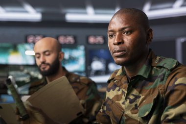 Military officers in war room reviewing reconnaissance battlefield files to prepare strategy. Close up of intelligence agency coworkers reading mission case file, getting debriefed on enemies