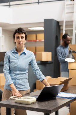 Masasındaki genç kadın teslimat hizmetleri için sevkiyat verilerini inceliyor, dağıtım için göndermeden önce depodaki kasetleri doğruluyor. Perakende açılışı için el paketleme malları.