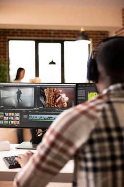 Rear view of male editor adjusting transitions and color grades during post production. African american creative professional wearing headphones while editing video footage at home studio.