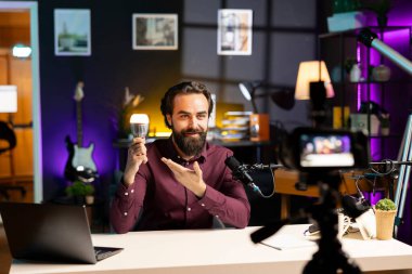 Neon ışıklı ev stüdyosundaki etkili profesyonel kamerayla çevrimiçi yayın platformları için akıllı ampul incelemesi çekiyor. Online yıldız filmleri özel ekipmanlı IoT ev otomasyon ürünü