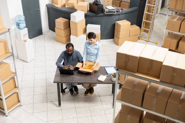 Emri işlemek ve envanteri yönetmek için birlikte çalışan çok ırklı depo çalışanları ve ticaret teslimat servisi. Bir grup insan depoda mal topluyor..