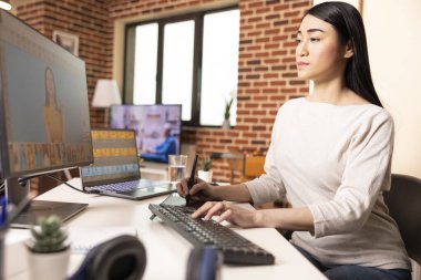 Asyalı grafik tasarımcısı dijital çizim defteriyle çalışıyor, resimleri rötuşluyor ve tasarım elemanlarını geliştiriyor. Yaratıcı ev stüdyosundaki bilgisayar ekranında görsel detayları mükemmelleştiren yetenekli fotoğraf editörü.