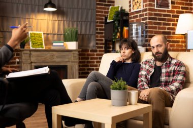 Caucasian couple seated on couch in therapist office during counseling session, seeking professional guidance for relationship issues. Portrait of boyfriend and girlfriend looking at camera.